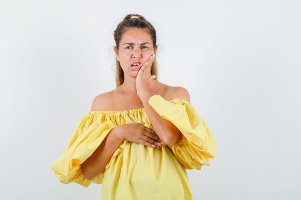 Млада жена държи ръката си върху бузата и изпитва болка в зъба.