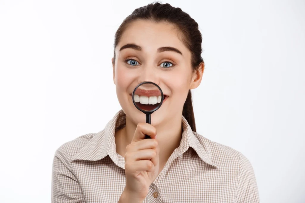 Млада , усмихната жена показва зъбите си през лупа.