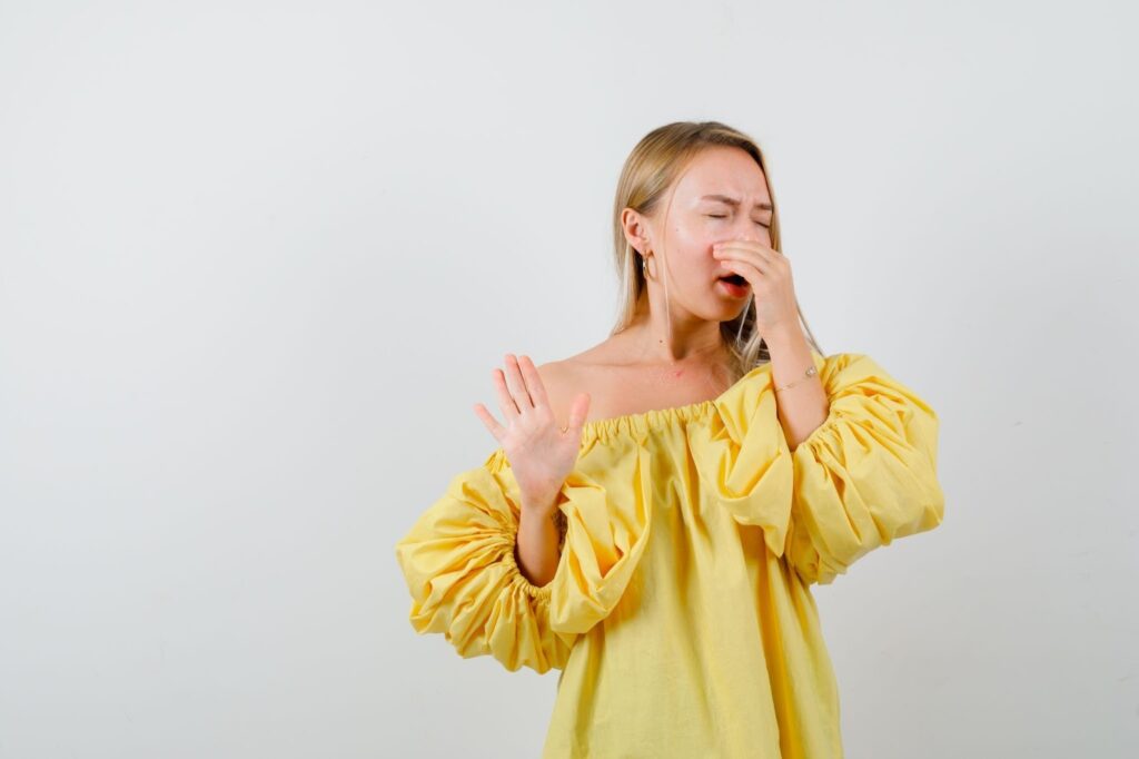 Руса жена, облечена в жълто, е затворила очи и запушила с ръка носа си.